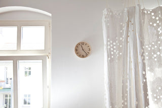 Natural wall clock with cream face and black hands on a white wall