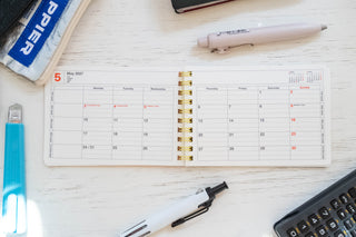 2027 May monthly calendar page in small notebook with gold spiral rings, open