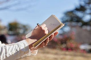 A5 square notebook cover, tan exterior, held in hand while writing