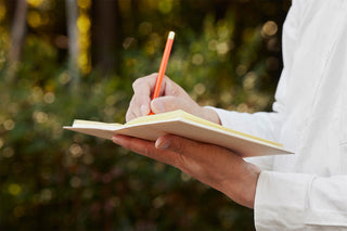 A5 square notebook cover with cream pages; writing with pencil