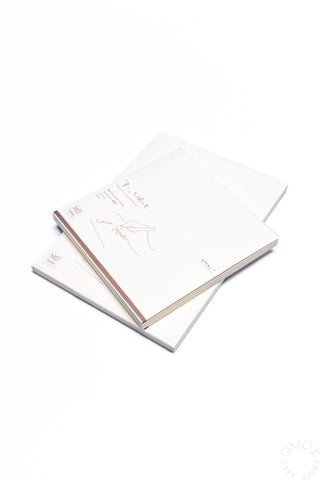 Open white cotton notebook with printed guide lines and brown-edged binding
