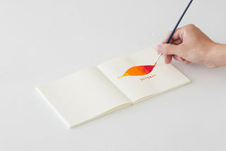 White cotton notebook opened flat with pencil writing on blank pages