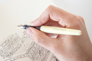 Cream fountain pen held in hand above paper, writing tip visible