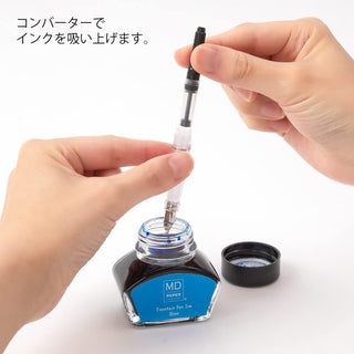 Hands filling an MD fountain pen converter from a blue ink bottle