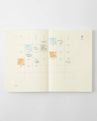 MD notebook monthly calendar spread with handwritten notes and colored date marks