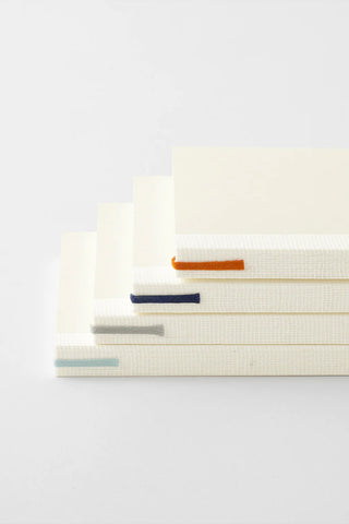 Stack of dot grid notebooks in cream with colored spine bands