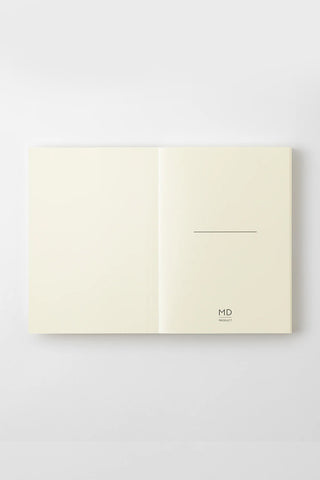 Cream notebook opened flat, two-panel cover with minimalist MD logo on right panel.