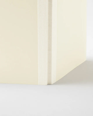 Cream notebook corner view, textured spine and page edge, blank pages.
