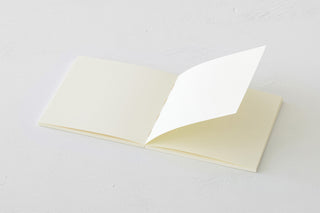 Thick cream notebook open with blank pages on both sides and visible inner sheets.