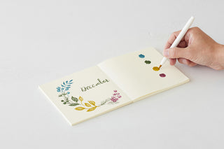 Thick notebook open to botanical “vbeeear” writing area with pen in hand