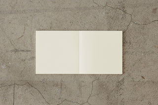 Thick cream notebook open, two blank pages visible with spine seam.