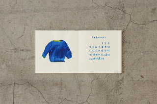 Thick cream notebook open to a blue sweater illustration and a calendar grid.