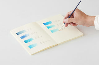 Thick cream notebook, open pages with blue notes as a pen writes on the sheet.
