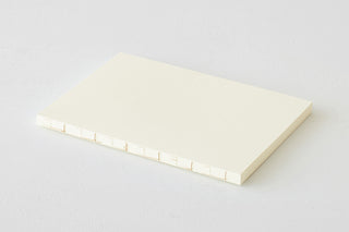 Thick cream notebook, closed and angled view showing the page thickness at the spine.