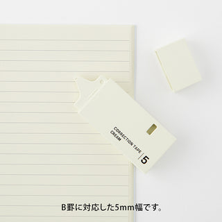 Correction tape dispenser, 5mm cream, angled over ruled paper