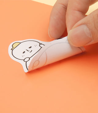 Single cute cartoon character sticker being peeled and pressed onto an orange surface
