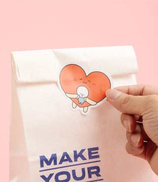 Orange heart character sticker being applied to a white envelope