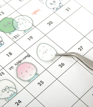 Macro view of character stickers on a grid, with a tweezer holding a pale blue face
