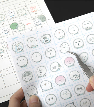 Sticker sheet filled with small round character faces and a hand holding a tweezer