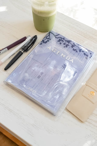 Blue A5 weekly vertical planner lying on desk, Agenda cover with pages visible