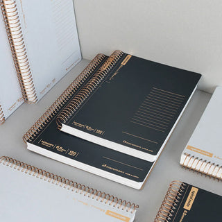Black A5 spiral notebook, open to ruled pages with copper rings on the spine