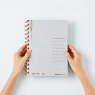 B5 spiral notebook open flat with ruled sheets, tan spine label, hands holding