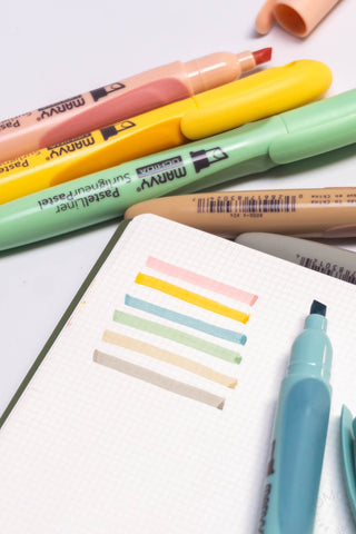 Pastel liner pens with colored tips over a notebook with colored swatch lines