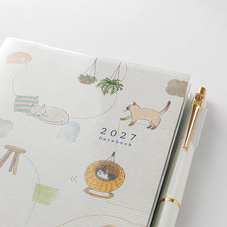 Close-up of 2027 cat-illustrated planner cover with pen and gold accents.