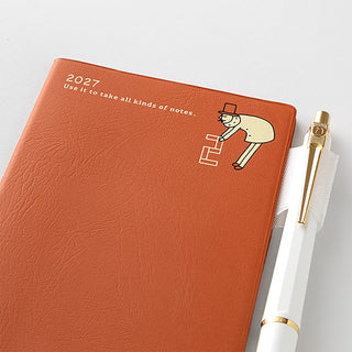Midori 2027 B7 monthly planner orange cover with character graphic beside a pen