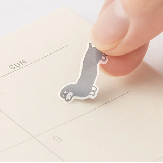Hand placing a dog-shaped planner sticker on a blank day grid