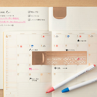 Copper clip ruler on planner with stencil pattern and mm scale, measuring tool