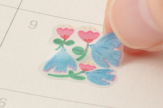 Heart-shaped floral sticker with blue flowers held by a fingertip