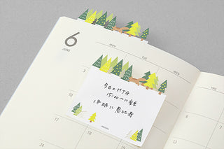 Forest-themed sticky note pad with tree graphics, placed on a calendar page