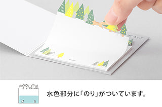 Hand pressing a forest tree sticky note onto a stack of memo pads