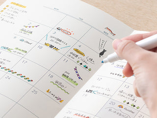 Hand using a black stamp on a paper calendar planner with colorful icons and notes.