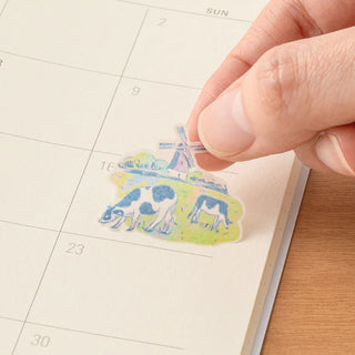 Hand placing a Dutch-themed sticker on a weekly planner date grid
