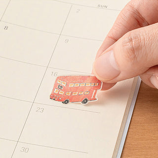 Hand placing a red bus sticker on a planner date grid