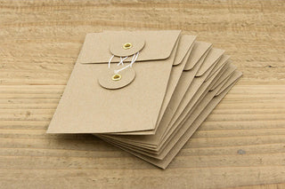 Stack of brown kraft envelopes with flap closure and two round tags tied with white string.