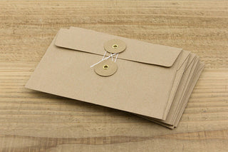 Two brown kraft envelopes stacked on wood, each with flap and round button-style closure.