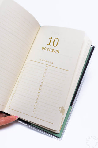 Beige 5-year diary with open pages and gold October date, navy edge binding visible