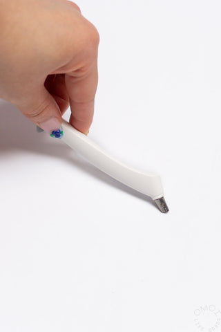 White scrapbook cutter with metal blade tip, held above paper