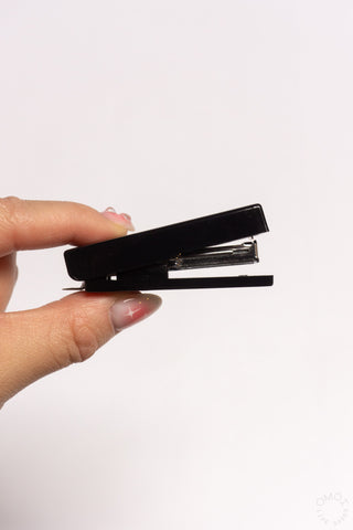 Black compact stapler with open top held by hand.