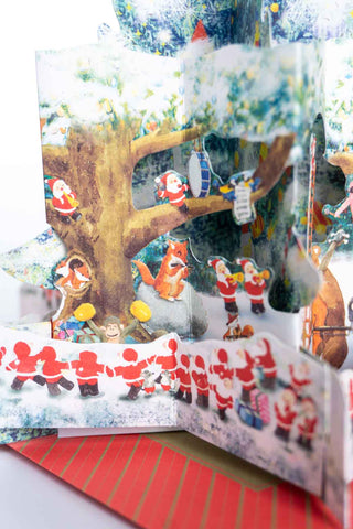 Snowy forest holiday pop-up card with Santa band under a decorated tree