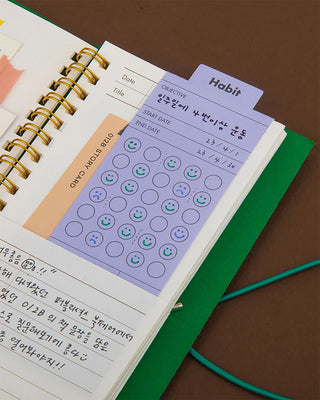 Open green habit tracker notebook page with smiley circle check grid and date fields