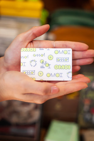 OMOI gift card with repeating OMOI icons, held by hand at chest height