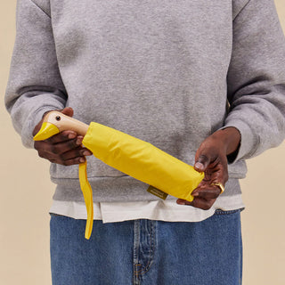 Hands holding yellow compact duck umbrella, folded sleeve and duck head handle
