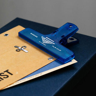 Blue plastic Clampy binder clip on dark folder