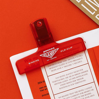 Red plastic binder clip clipped to printed paper