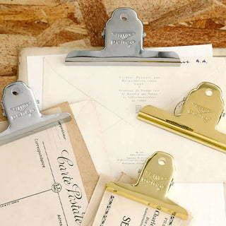 Set of silver and gold steel binder clips with engraved handles on papers