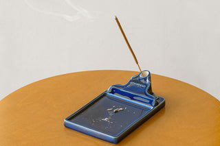 Navy ceramic incense holder tray with incense stick and small ash residue inside.